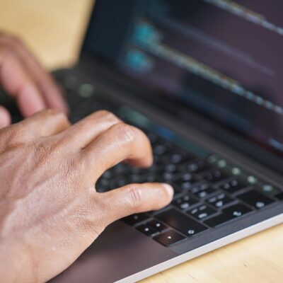 Hands typing on a laptop with code displayed on screen, showcasing technology use.